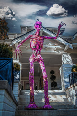 Giant purple skeleton monster with pumpkin head stands on steps  towering over vintage home decorated for Halloween