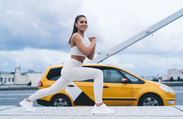 Young happy woman makes deep forward lunges to pump muscles of the legs and buttocks, simple and effective exercises during morning workout in city. Healthy lifestyle,  female keeping body in shape