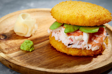 Pan-Asian cuisine concept. Japanese sushi burger made from rice bread, crab meat, avokado and wasabi sauce. Serving on wooden board. copy space