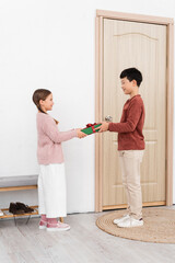 Side view of smiling asian boy giving present to friend near door at home