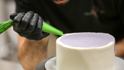 cake designer squeezing piping bag with lilac glaze filling decorating top sweet