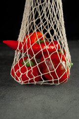 Red and orange peppers in a string bag on a dark background. Vegetables in a string bag