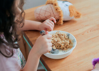 a girl is eating oatmeal breakfast at the kitchen table surrounded by toys