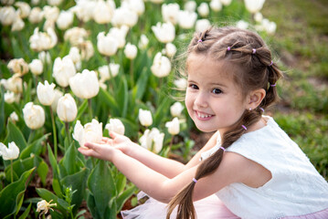portrait of smiling happy brunette girl in white dress in  in summer park with beautiful tulips...
