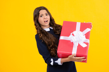 Angry teenager girl, upset and unhappy negative emotion. Child teen girl 12-14 years old with gift on yellow isolated background. Birthday, holiday present concept.