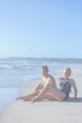 happy modern mother and teenage daughter sitting at beach