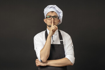 the chef on a black background shows the sign quietly to the camera. silence concept