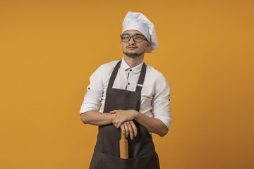 a young chef man in a black apron, beret and glasses stands with knives in his hands against a colored background