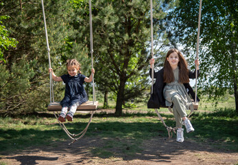 two girls sister on swing in summer park