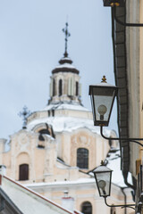Fototapeta na wymiar Beautiful narrow street in Vilnius Old Town with Dominican Church of the Holy Spirit, old buildings and street lamps in winter covered by the snow, vertical