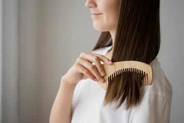A teenage girl combs her hair with a wooden comb. Taking care of hair and ecology.