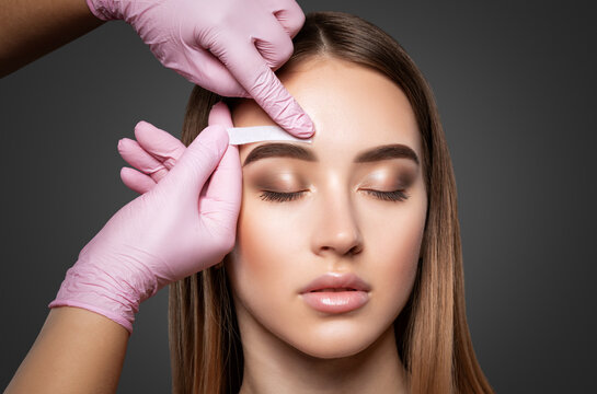 Makeup artist does facial hair removal procedure. Beautiful girl having Permanent Make-up on her Eyebrows. The make-up artist does Long-lasting styling of the eyebrows