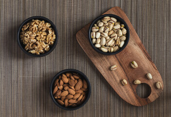 Three different bowls with almonds, walnuts and pistachios over a wooden tablecloth.