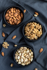 Almonds, walnuts and pistachios in three different bowls on a tablecloth with scattered nuts. Top view.