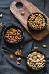 Perspective close up view of a fatty foods. Almonds, walnuts and pistachios in bowls on tablecloth and wooden tableboard.