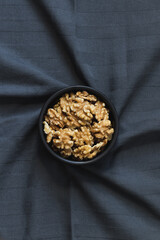 Top view of a centered bowl with walnuts over a twisted tablecloth.