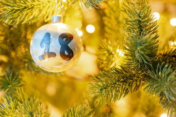 eine weiße Weihnachtskugel am Christbaum, mit einer Zahl (18) für den Adventskalender