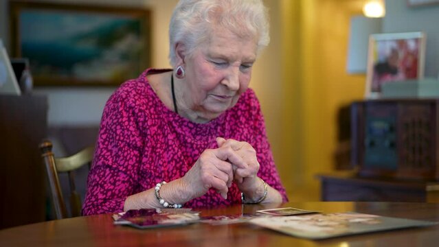 Elderly senior woman smiling and sitting at table looking at photo memories.