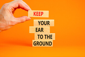 Keep your ear to the ground symbol. Concept words Keep your ear on the ground on wooden blocks. Businessman hand. Beautiful orange background. Business keep your ear on the ground concept. Copy space.