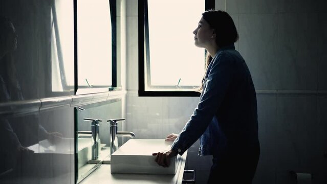 Dramatic scene of a woman standing in front of bathroom mirror looking at self