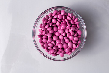 Pink candy coated chocolate button sprinkles in a bowl on marble - M&Ms, Smarties, sprinkles