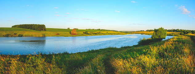 Summer sunny panoramic landscape with blue calm river and green farm fields