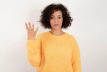 young beautiful woman with curly short hair wearing yellow sweater over white background smiling and looking friendly, showing number four or fourth with hand forward, counting down