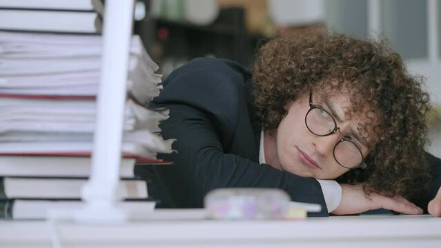 Nerdy male office employee lying on desk, huge pile of papers, work overload