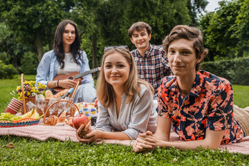 Portrait of four young friend having time together at picnic with some food and drink.
