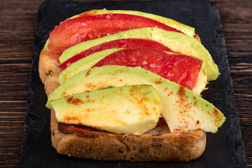 Grain bread sandwich with slices of tomato and avocado and coarse salt.