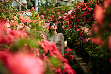 A girl in a light brown dress and glasses in a garden of blooming azaleas