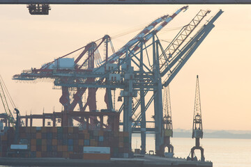 Obraz premium Sea cargo cranes in the port terminal of Lisbon, silhouette on sunrise