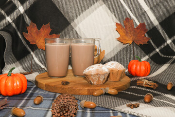 Warm and delicious cocoa with marshmallows and cupcakes with sugar sprinkles. Autumn drink among warm blankets, cones, acorns and yellow leaves