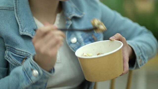 Focus on paper container with caesar salad in young woman hands. Girl eats fresh salad at the food court