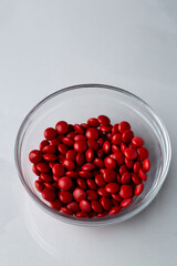 Red candy coated chocolate button sprinkles in a bowl on bright marble - M&Ms, Smarties, sprinkles