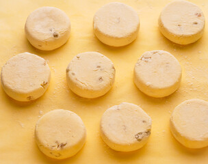 Raw frozen round Syrniki with dried apricots on a yellow background. Semi-finished products for homemade breakfast