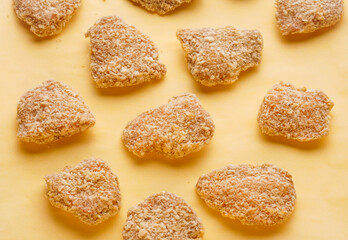 Semi-finished products for homemade nuggets. Raw frozen pieces of breaded chicken on a yellow background.