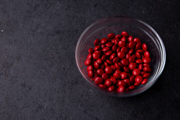 Red candy coated chocolate button sprinkles in a bowl on dark slate - M&Ms, Smarties, sprinkles