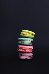 Close-up on a black background macaroons folded in the form of a pyramid in different colors of lilac, pink, blue and green, copy space.