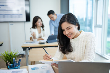 Obraz premium Beautiful Asian businesswoman secretary working happily in office using laptop and diligently taking notes.