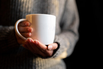 a girl in a knitted sweater holds a white mug with a hot drink tea