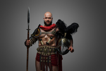 Shot of serious roman gladiator with naked torso holding long spear and plumed helmet.