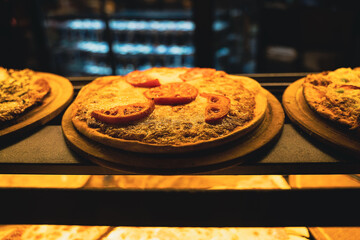 different kinds of pizza on wooden plates on the shelves of street food shop window