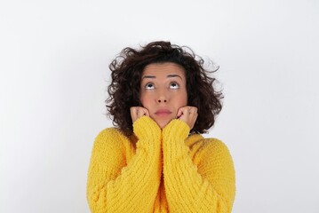 Portrait of sad young beautiful woman with curly short hair wearing yellow sweater over white...