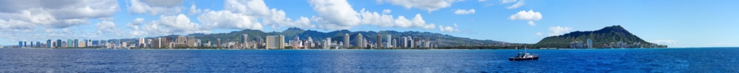 Fototapeta na wymiar Wide panoramic view of Honolulu as seen from a boat off Waikiki in Hawaii - Modern American city skyline on the O'ahu volcanic island in the middle of the Pacific Ocean