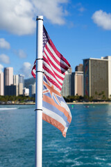 Hawaiian flag next to the flag of the United States flying in the wind on a boat off Honolulu in Hawaii - Flags facing Waikiki Beach on O'ahu island - obrazy, fototapety, plakaty
