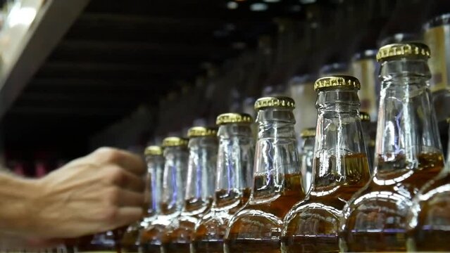 A long row of beer bottles on a store shelf and a customer takes a couple