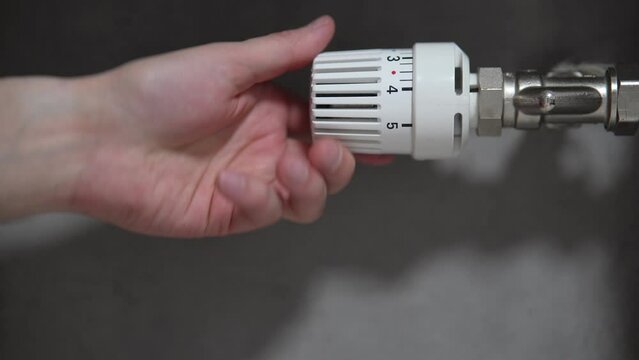 Hand adjusting temperature on heating radiator thermostat, saving energy by adjusting heating thermostat. 
