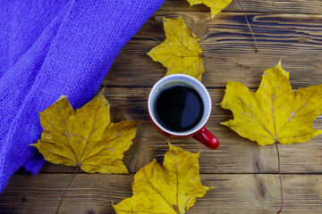 Cosy knitted blue sweater, cup of coffee and autumn maple leaves on wooden table. Top view. Autumn...