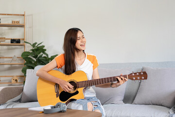 Young woman is practice basic guitar chords and playing guitar with pop songs while sitting on comfortable